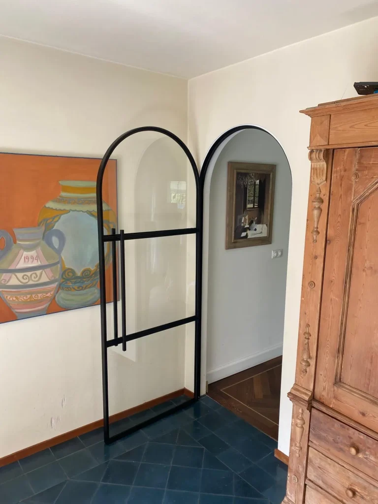 "Scharnierdeur met ronde bovenakant, glas en zwarte kozijnen."