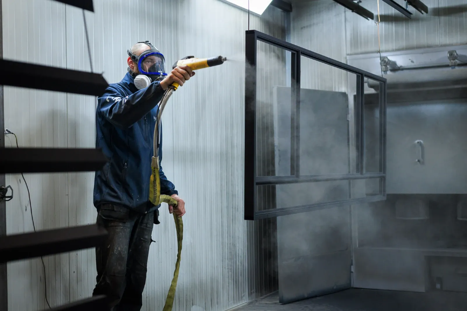 Een coater is aan het werk en spuit een stalen deur zwart